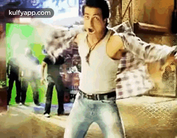a man in a white tank top and blue jeans is dancing on a street .