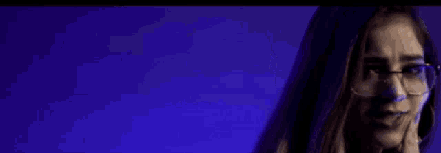 a woman wearing glasses is holding her hair in front of a blue background and laughing .