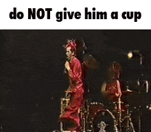 a man in a red suit is jumping in the air in front of a drum set with the caption do not give him a cup