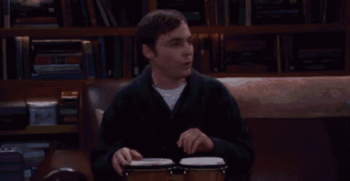 a man is sitting on a couch playing a pair of bongos .