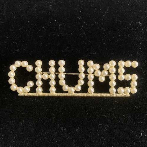 a brooch with the word chillis made of pearls is on a black surface .