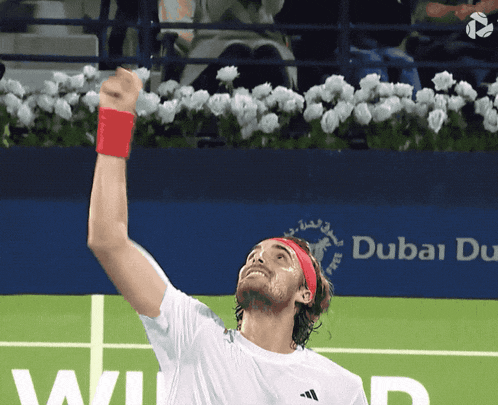 a tennis player holds his fist up in the air in front of a dubai du logo