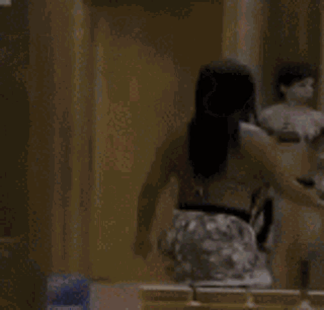 a woman in a bikini is standing in front of a mirror looking at herself .