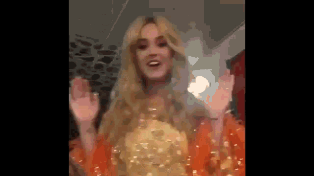 a woman in a gold dress is waving her hands .
