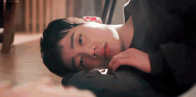 a young man is laying on the floor with his head on his hand and looking at the camera .