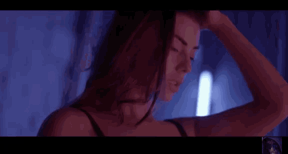 a woman in a black bra is standing in a dark room with her hand on her forehead .