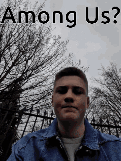 a man in a denim jacket is standing in front of a fence with the words among us written above him