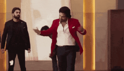 a man in a red jacket is dancing in a room with other men