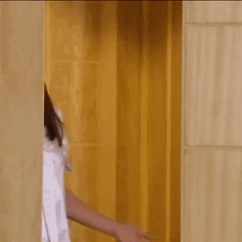 a woman in a white robe is peeking out from behind a wall .