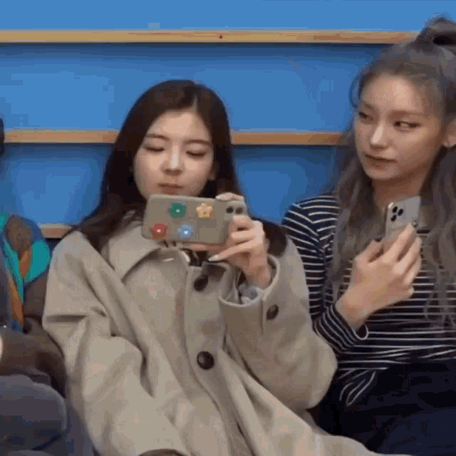 two women are sitting next to each other looking at their phones