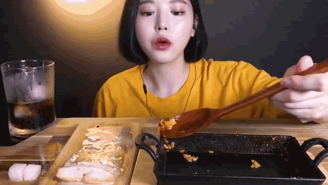 a woman in a yellow shirt is holding a wooden spoon over a pan of food ..