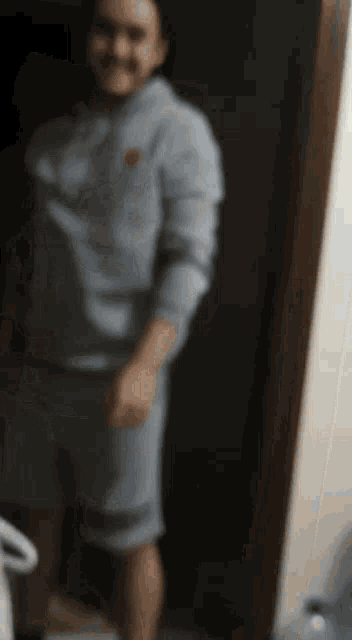 a man in a blue hoodie and shorts is standing in a doorway .