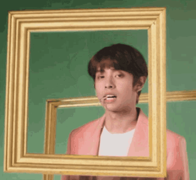 a young man in a pink jacket is holding a picture frame in front of his face