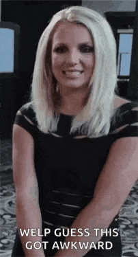 a woman in a black dress is smiling and looking at the camera while standing in front of a window .