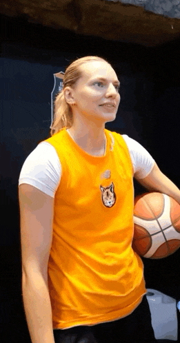a woman wearing an orange shirt with a cat on it holds a basketball