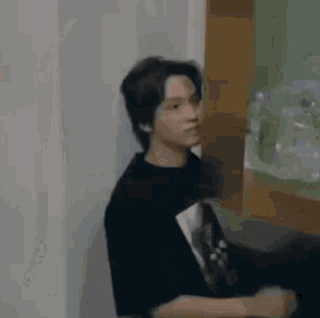 a young man in a black shirt is standing in front of a wooden cabinet .