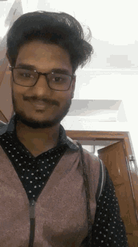 a man wearing glasses and a polka dot shirt looks down at the camera
