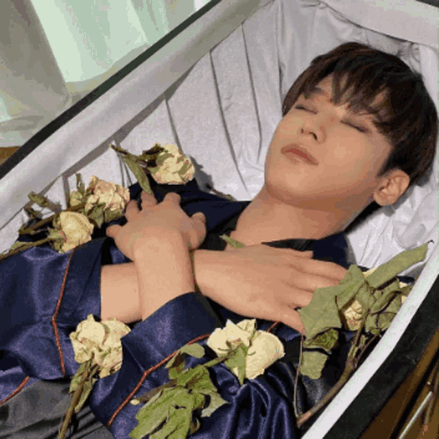 a young man is laying in a coffin with flowers around his neck