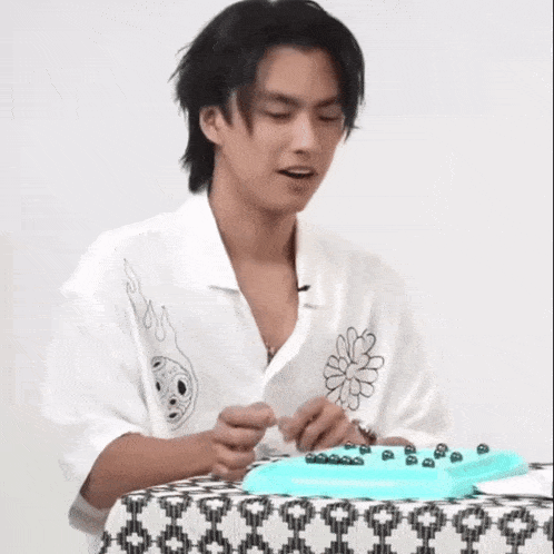 a man in a white shirt is sitting at a table with a blue tray of beads on it .