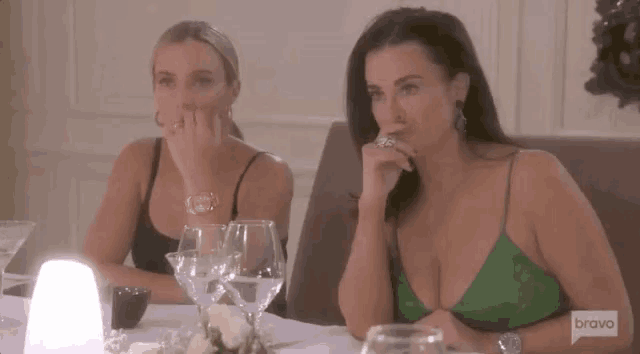 two women are sitting at a table with wine glasses and flowers .