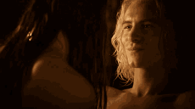 a man with long blonde hair looks at a woman