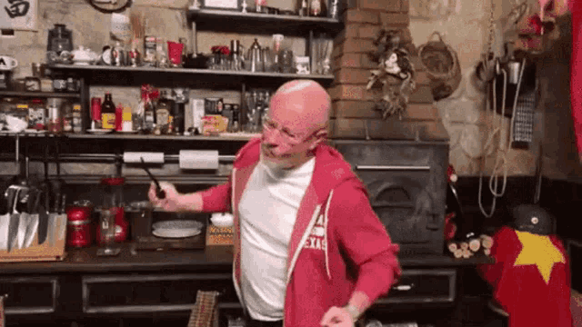 a bald man in a red hoodie is holding a magic wand in a kitchen .
