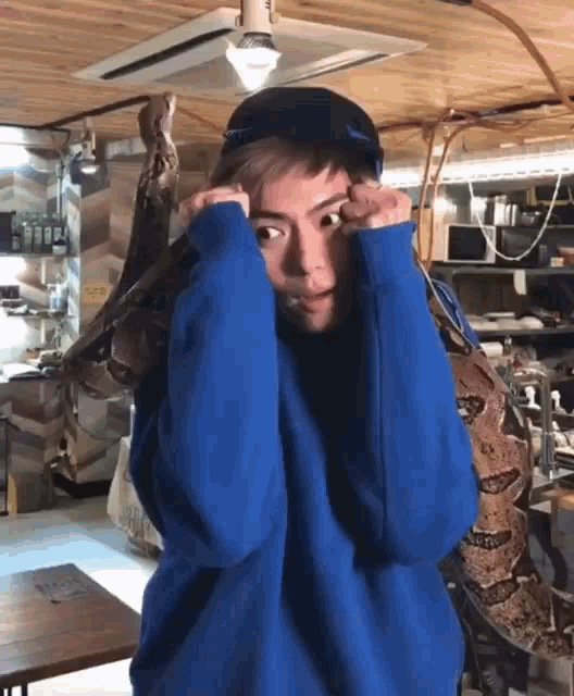 a man in a blue sweater is holding a large snake around his neck .