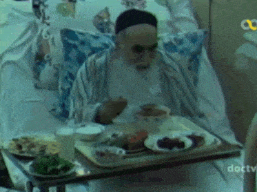 a man is sitting in a hospital bed with a tray of food in front of him that says doctv