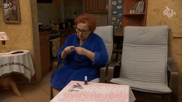 a woman in a blue robe sits at a table with a bottle of nail polish