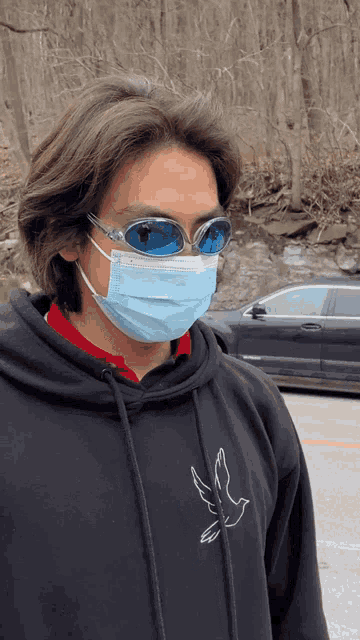 a man wearing a face mask and sunglasses is standing in front of a car
