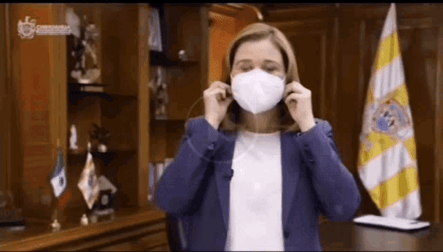 a woman in a blue jacket is putting on a mask in front of a mexican flag .