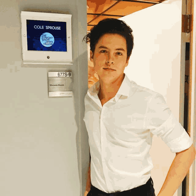 a man in a white shirt stands in front of a sign that says cole sprouse
