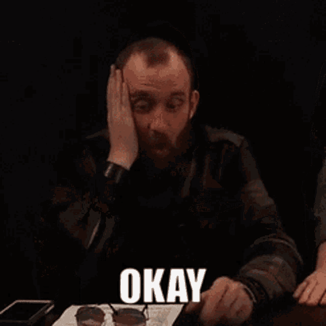 a man with a beard is sitting at a table with the words that i get written on a piece of paper