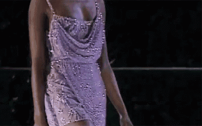 a woman in a purple dress is walking down a runway in a dark room .