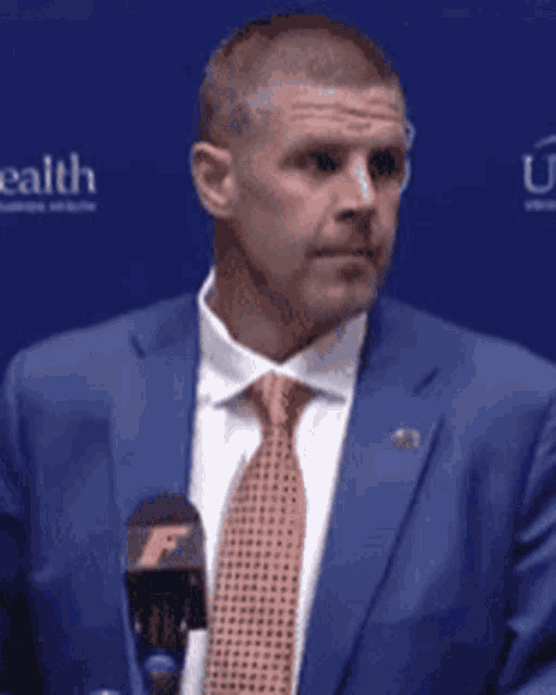 a man in a blue suit and orange tie stands in front of a microphone