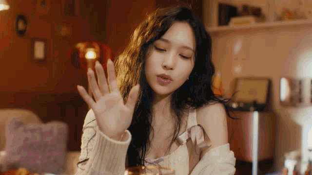 a woman in a white sweater is sitting at a table with her hand out .