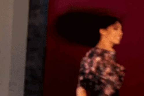 a woman in a floral dress is standing in front of a wall with a picture on it .