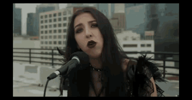 a woman in a black dress is singing into a microphone on a rooftop .