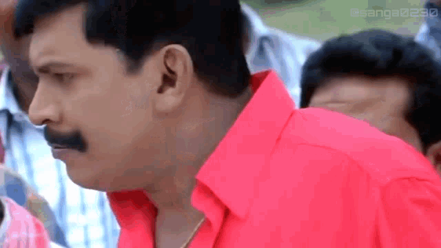a man in a red shirt with a mustache is standing in a crowd of people .