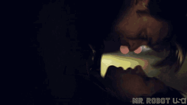 a man and a woman are kissing in a dark room with the words mr robot usa in the corner .