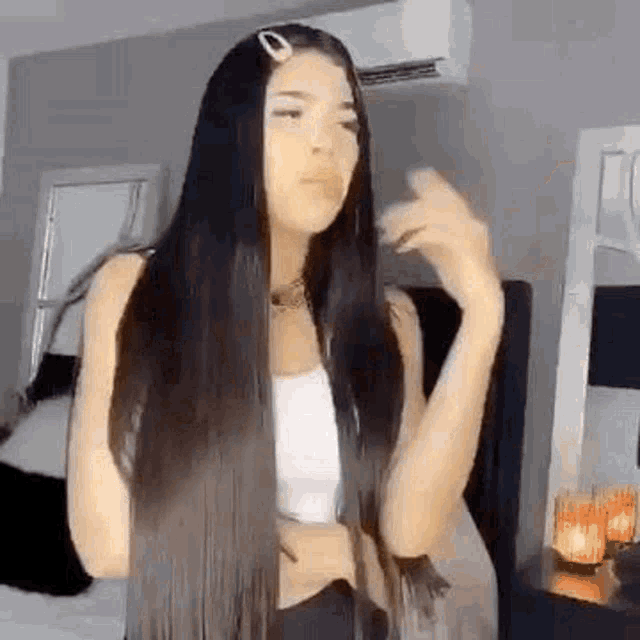 a woman with long black hair is wearing a white tank top and black pants .