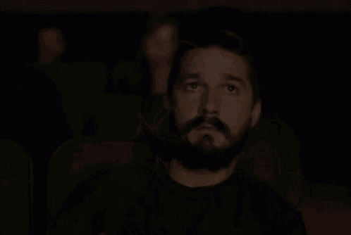 a man with a beard is covering his mouth while watching a movie in a dark theater .