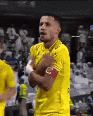 a soccer player in a yellow jersey is standing on a field with his hands in his pockets .