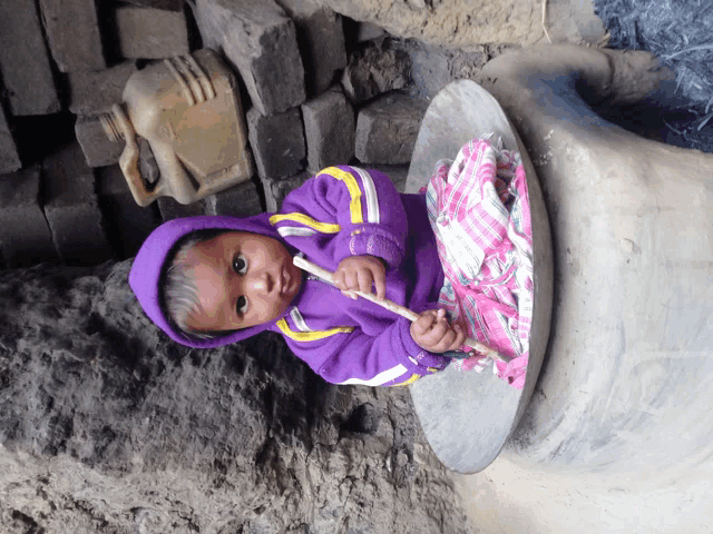 a little girl in a purple hoodie sits on a table