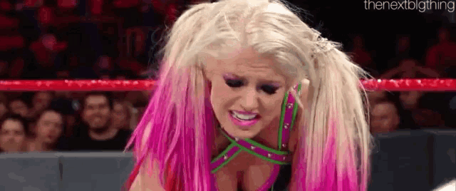 a woman with pink hair is kneeling down in a ring .