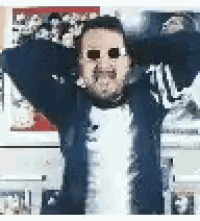 a man wearing sunglasses is standing with his arms outstretched in front of a wall with pictures on it .