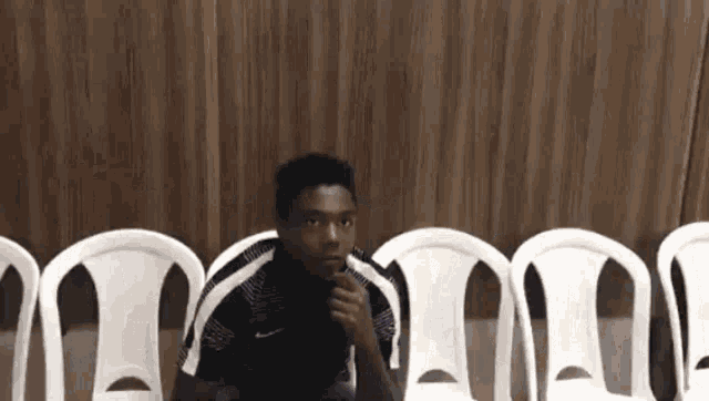 a young man is sitting in a row of white chairs and thinking .