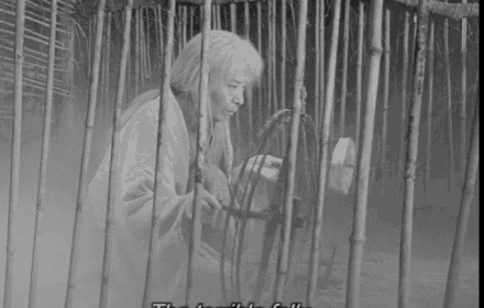 a black and white photo of a man sitting in a cage looking at a spool of thread .