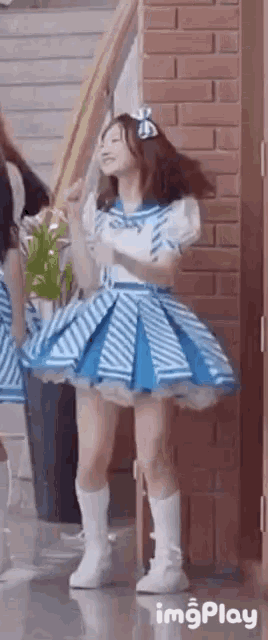 a woman in a blue and white striped dress is standing in front of a brick wall .