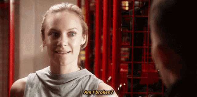 a woman is smiling and talking to a man in a gym while asking if she is broken .